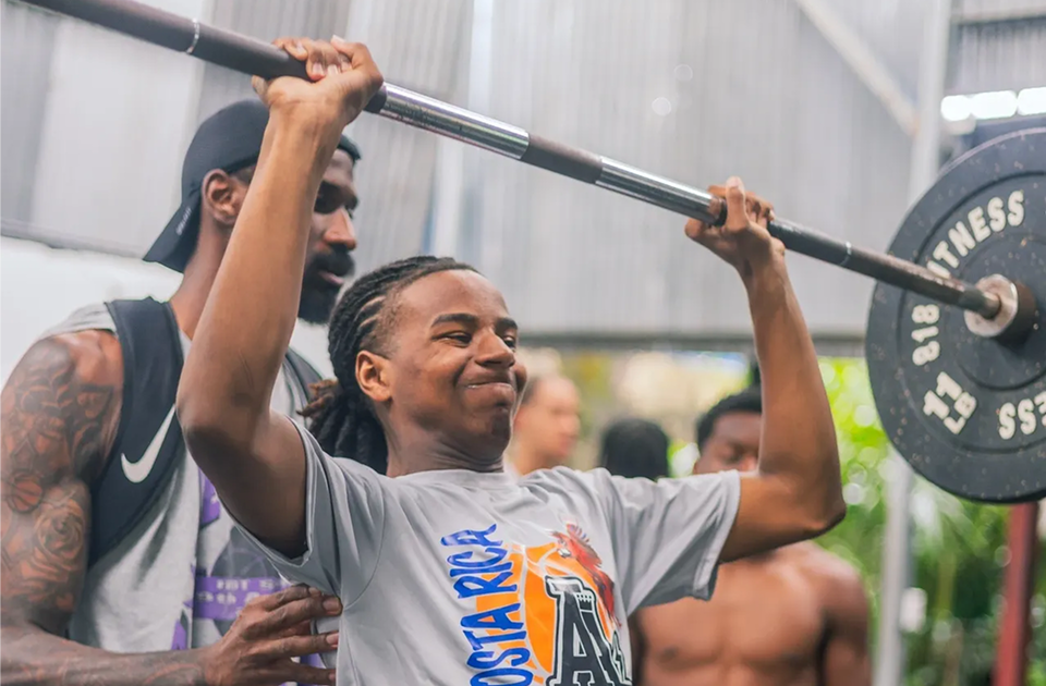 Young woman lifting weights with a trainer's support.